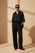 Model wearing an all-black oversized short-sleeve shirt with black trousers